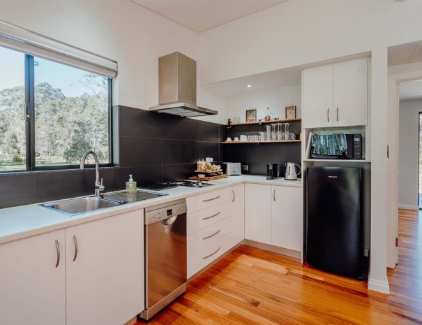 The kitchen in the chalets. There is a microwave oven, refrigerator, kettle, Nespresso machine, toaster, breakfast hamper, gas cooktop with rangehood, dishwasher, sink and cupboards.