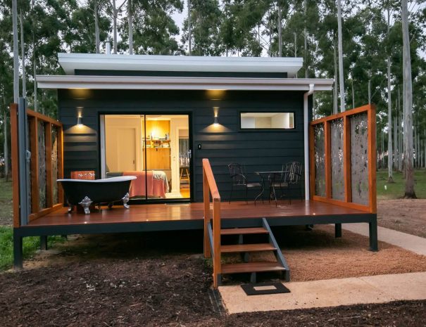 An image showing the back deck of the chalet. There is a clawfoot bath on the back deck and an outdoor setting. The rosegum trees are in the background.