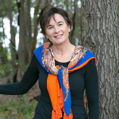 A woman standing near a tree and smiling. She is one of the owners of Tree Chalets