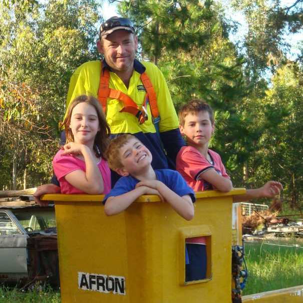 Owner Andrew Robinson operating a cherry picker machine which is used to trim the lower branches of the Rosegum trees. There are 3 children with him.