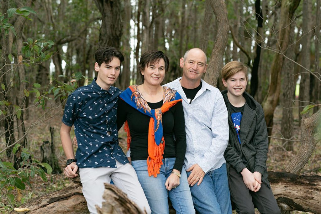 A portrait of the Robinson family. The image includes the owners, Andrew and Fran, with their two sons. They are all sitting on a log with the trees in the background.