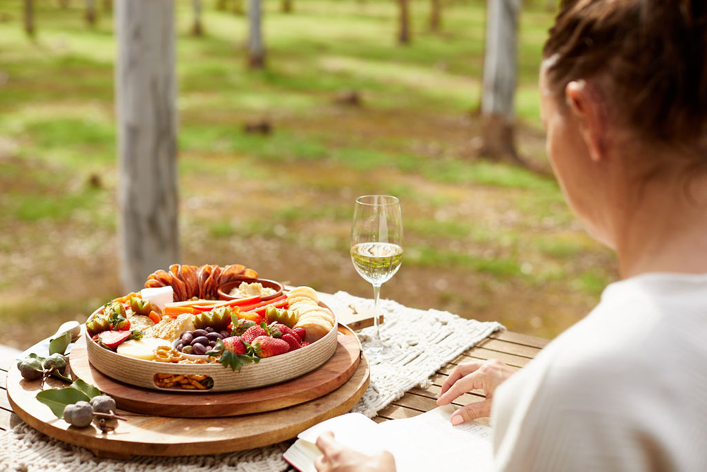 lady enjoying a Grazing board and glass of white wine amongst the trees